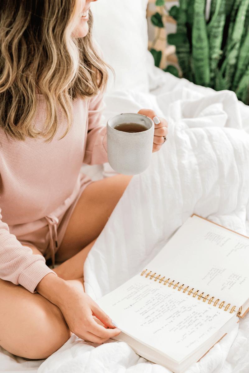 woman holding oolong tea cup in bed with notebook