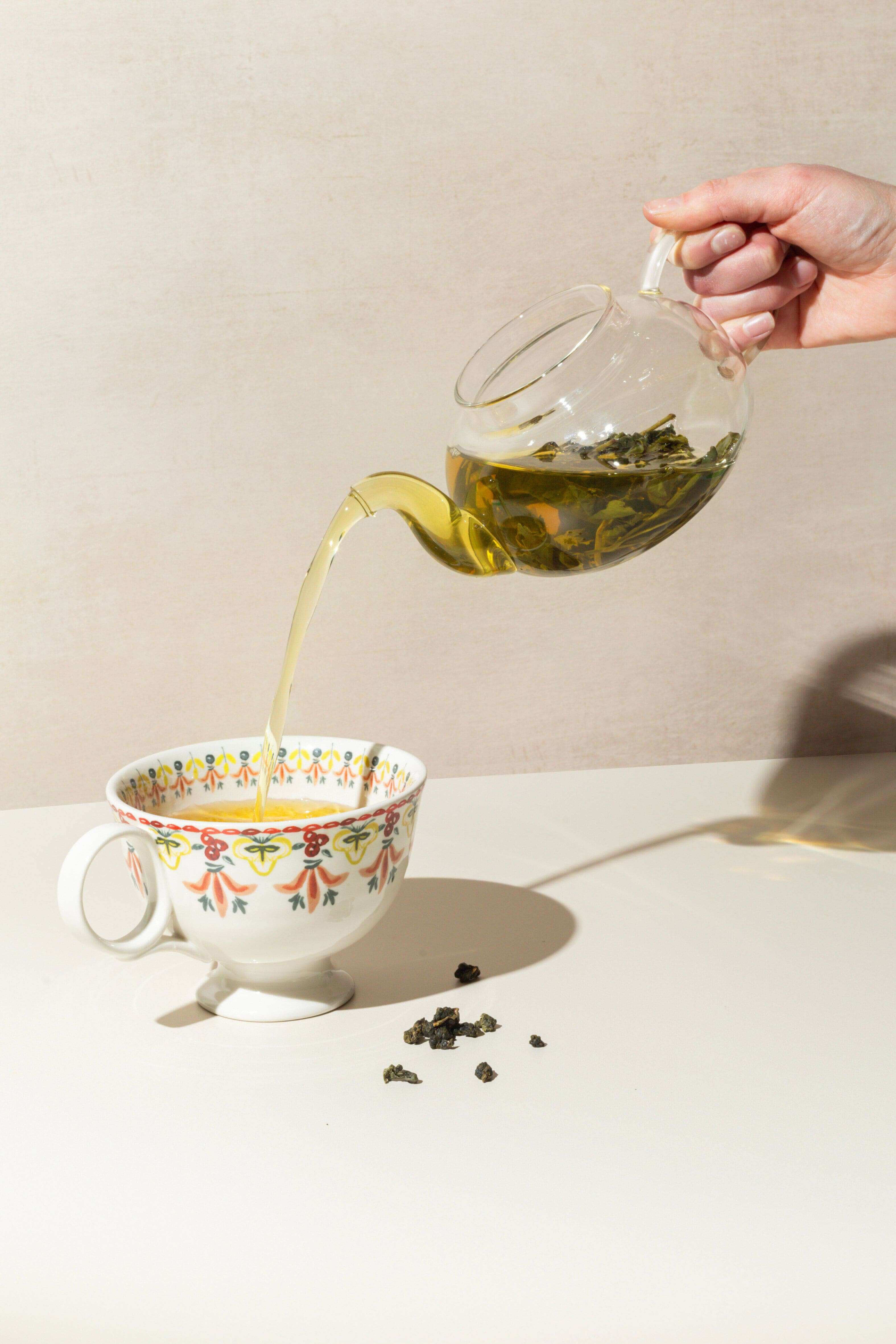 hand pouring oolong tea into teacup from glass teapot